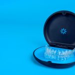 Black plastic case with transparent braces on blue background. Insivible removable retainers for orthodontic treatment.